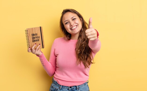 Mujer bonita hispana sintiéndose orgullosa sonriendo positivamente con los pulgares hacia arriba concepto de reciclaje