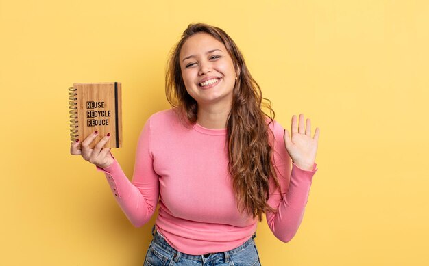 mujer bonita hispana sonriendo alegremente, saludando con la mano, dándote la bienvenida y saludándote. concepto de reciclaje