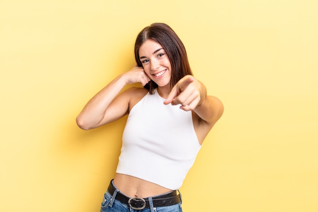 Mujer bonita hispana sonriendo alegremente y señalando a la cámara mientras hace una llamada que luego gesticula, hablando por teléfono