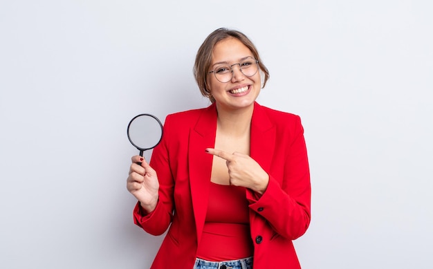 Mujer bonita hispana sonriendo alegremente sintiéndose feliz y apuntando al concepto de lupa lateral