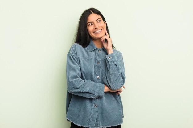 Mujer bonita hispana sonriendo alegremente y soñando despierto o dudando mirando hacia un lado