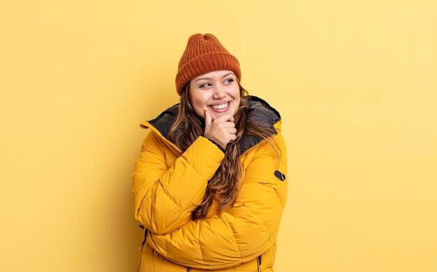 Mujer bonita hispana sonriendo con una expresión feliz y segura con la mano en la barbilla. ropa de invierno