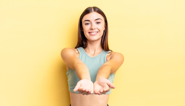 Foto mujer bonita hispana sonriendo felizmente con mirada amistosa, segura y positiva, ofreciendo y mostrando un objeto o concepto