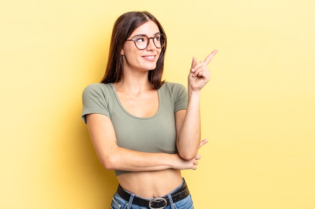 Mujer bonita hispana sonriendo felizmente y mirando hacia los lados, preguntándose, pensando o teniendo una idea