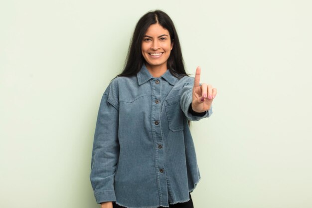 Mujer bonita hispana sonriendo y luciendo amigable mostrando el número uno o primero con la mano hacia adelante contando hacia atrás