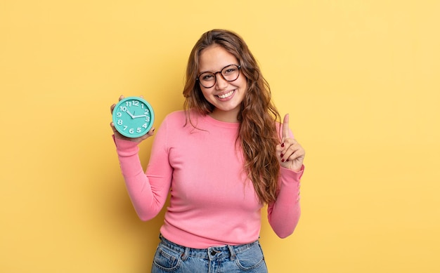 Mujer bonita hispana sonriendo y mirando amigable, mostrando el número uno. concepto de reloj despertador