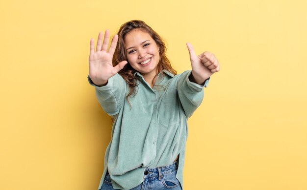 Mujer bonita hispana sonriendo y mirando amistosamente, mostrando el número seis o sexto con la mano hacia adelante, contando hacia atrás