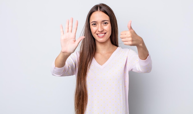 Mujer bonita hispana sonriendo y mirando amistosamente, mostrando el número seis o sexto con la mano hacia adelante, contando hacia atrás