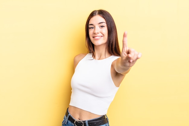 Mujer bonita hispana sonriendo con orgullo y confianza haciendo la pose número uno triunfalmente, sintiéndose como un líder