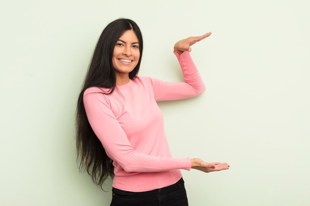 Mujer bonita hispana sonriendo sintiéndose feliz positiva y satisfecha sosteniendo o mostrando un objeto o concepto en el espacio de la copia