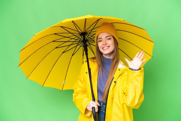 Mujer bonita joven con abrigo impermeable y paraguas sobre fondo de clave de croma aislado contando cinco con los dedos