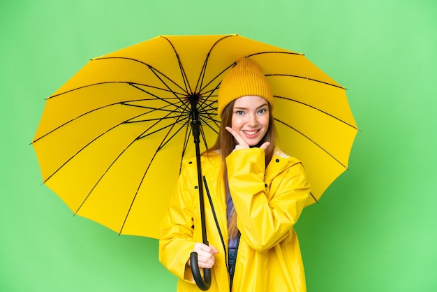 Mujer bonita joven con abrigo impermeable y paraguas sobre fondo clave de croma aislado feliz y sonriente