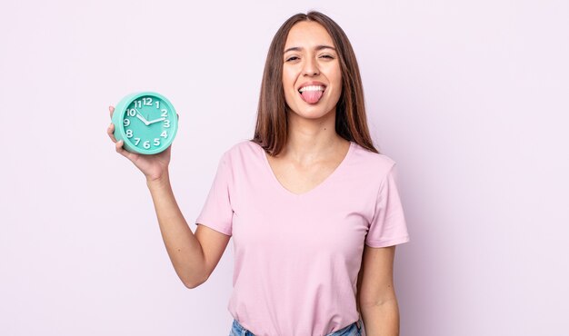 Mujer bonita joven con actitud alegre y rebelde, bromeando y sacando la lengua. concepto de reloj despertador