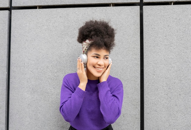 Mujer bonita joven, afro de raza mixta, en la calle con auriculares sonriendo feliz