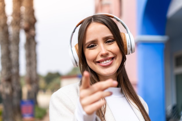 Mujer bonita joven al aire libre escuchando música y apuntando hacia el frente