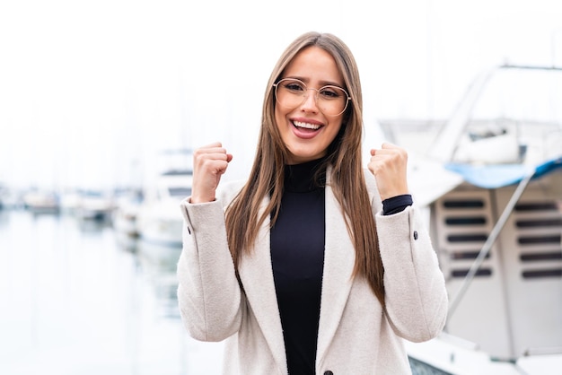 Mujer bonita joven al aire libre con gafas y celebrando una victoria