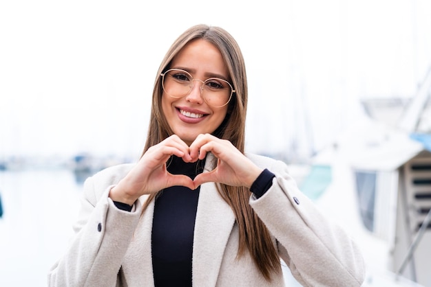 Mujer bonita joven al aire libre con gafas haciendo corazón con las manos