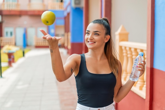 Mujer bonita joven al aire libre con una manzana y con una botella de agua