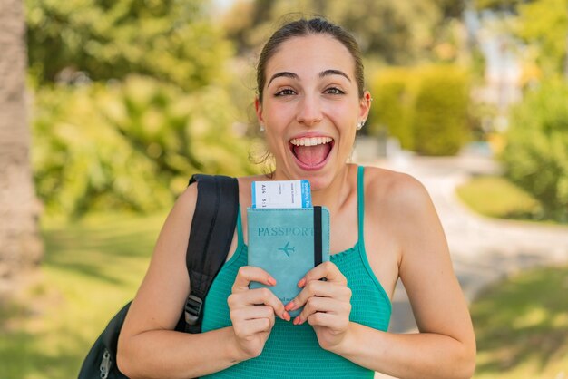 Mujer bonita joven al aire libre sosteniendo un pasaporte con expresión sorprendida