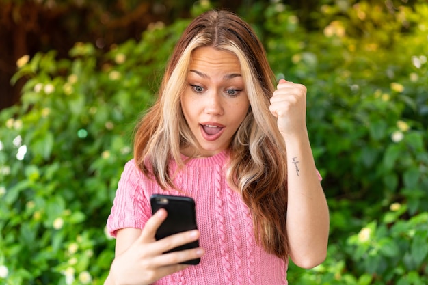 Mujer bonita joven al aire libre con teléfono móvil y haciendo el gesto de la victoria