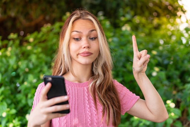 Mujer bonita joven al aire libre mediante teléfono móvil y levantando el dedo