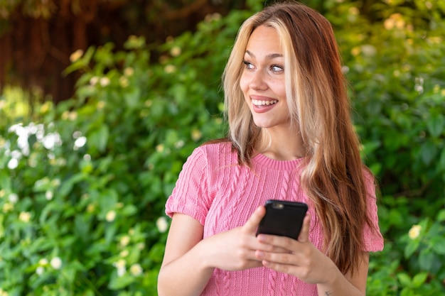 Mujer bonita joven al aire libre mediante teléfono móvil y mirando hacia arriba