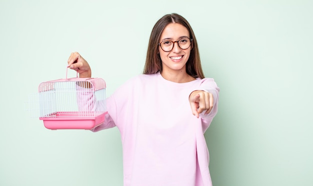 Mujer bonita joven apuntando a la cámara eligiéndote. concepto de jaula para mascotas