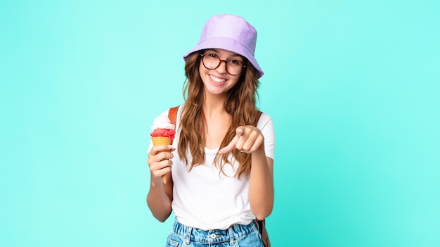 Mujer bonita joven apuntando a la cámara eligiéndote sosteniendo un helado. concepto de verano