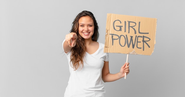 Mujer bonita joven apuntando a la cámara eligiéndote y sosteniendo una pancarta de poder femenino