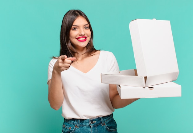 Mujer bonita joven apuntando o mostrando y sosteniendo pizzas para llevar y sosteniendo pizzas para llevar