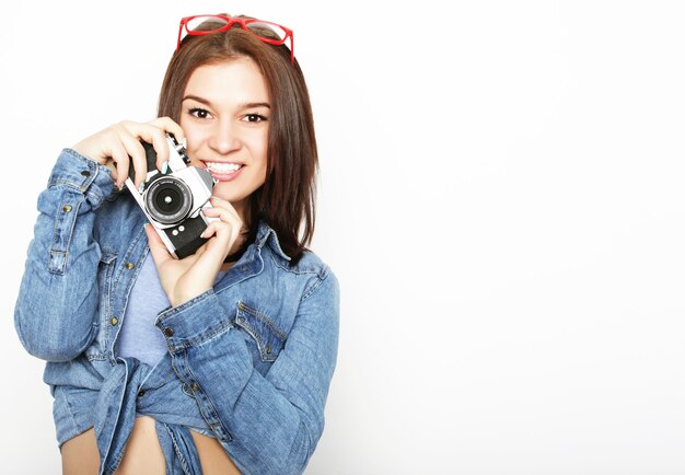 Mujer bonita joven asombrada que sostiene la cámara sobre el fondo blanco.