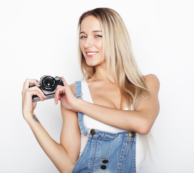 Mujer bonita joven asombrada que sostiene la cámara sobre el fondo blanco.