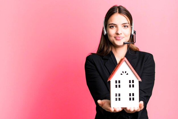 Mujer bonita joven con auriculares y un concepto de bienes raíces modelo de casa