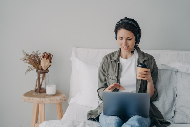 Mujer bonita joven con auriculares tiene una reunión en línea en casa Ocio y comunicación en cuarentena