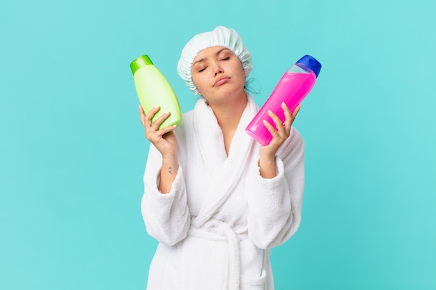 Mujer bonita joven con bata de baño y sosteniendo una botella de producto limpio