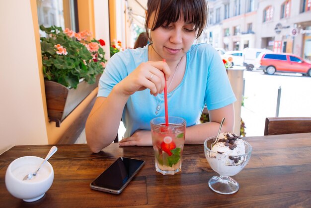 Mujer bonita joven bebe bebidas frías en el café exterior horario de verano