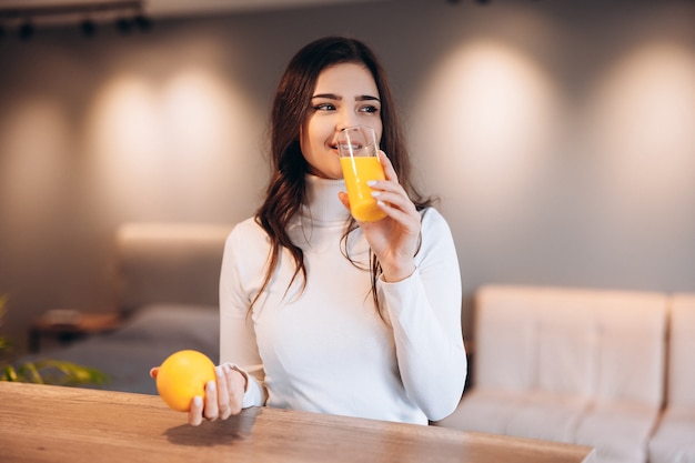 Foto mujer bonita joven está bebiendo jugo de naranja en la cocina de casa.