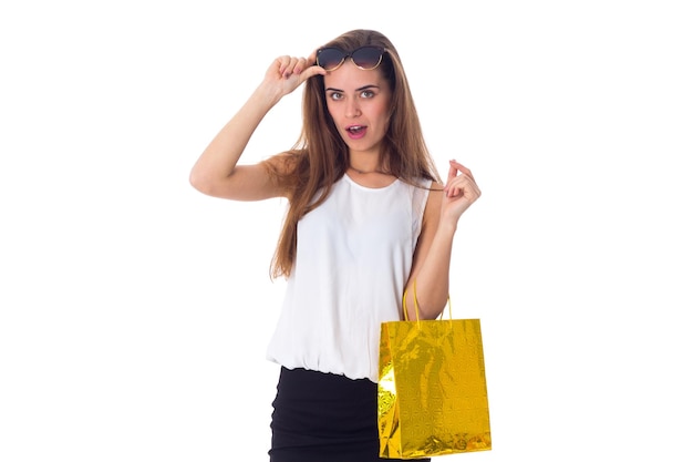 Mujer bonita joven en blusa blanca y falda negra con gafas de sol oscuras sosteniendo una bolsa de compras sobre fondo blanco en el estudio