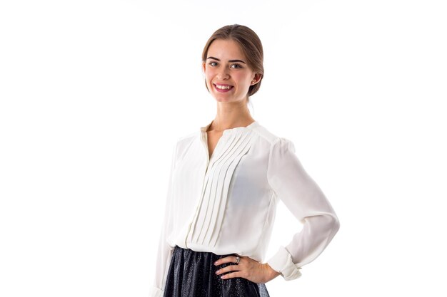 Mujer bonita joven en blusa blanca de pie y sonriendo sobre fondo blanco en estudio