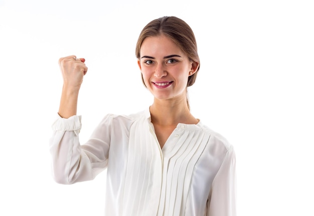 Mujer bonita joven en blusa blanca sonriendo y mostrando su puño sobre fondo blanco en el estudio