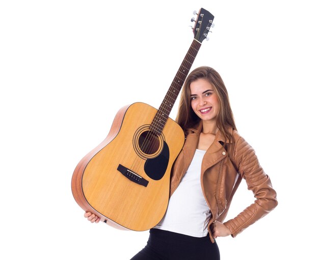 Mujer bonita joven con cabello largo en chaqueta y pantalón negro sosteniendo una guitarra y haciendo muecas