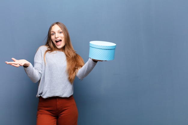 Mujer bonita joven con una caja azul sobre la pared azul con un espacio de copia