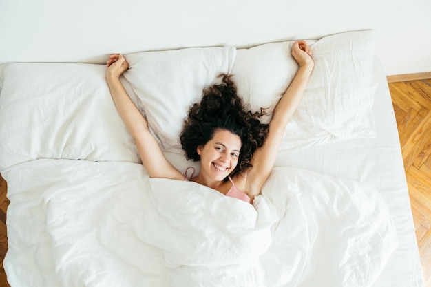 Mujer bonita joven en la cama con sábanas blancas luz brillante