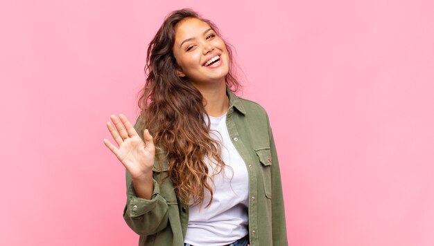 Mujer bonita joven con camisa abierta de mezclilla verde posando en la pared rosa