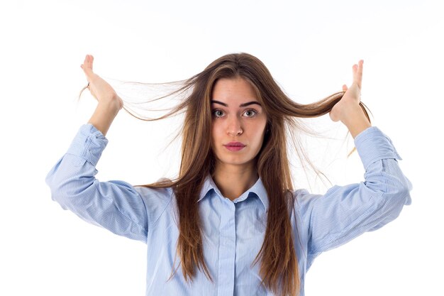 Mujer bonita joven con camisa azul recogiendo su largo cabello castaño sobre fondo blanco en el estudio