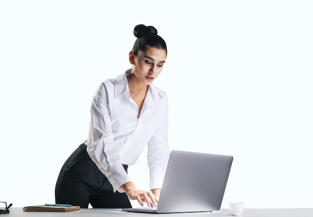 Mujer bonita joven con camisa blanca escribiendo en el teclado de un portátil moderno aislado en un primer plano de fondo de pared de luz abstracta