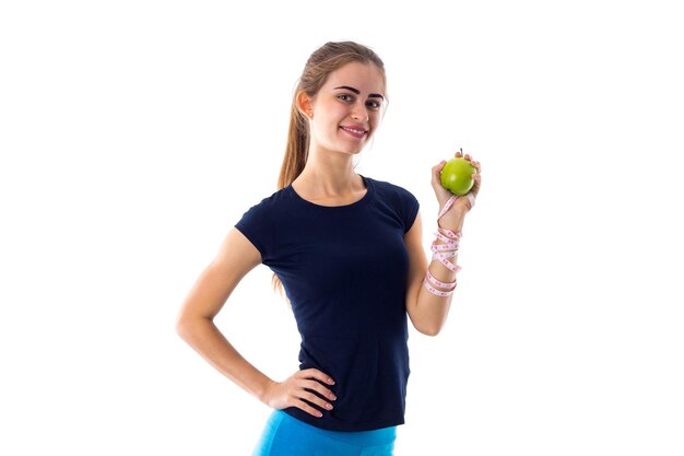 Mujer bonita joven en camiseta azul con centímetro alrededor de su cuello mordiendo manzana verde en estudio