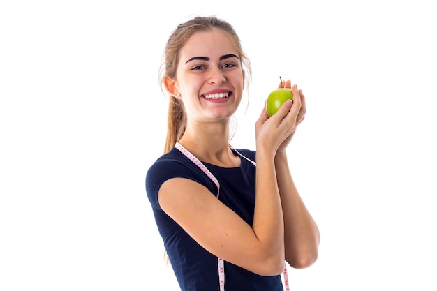 Mujer bonita joven en camiseta azul con centímetro alrededor de su cuello sosteniendo manzana verde cerca de la cara sobre fondo blanco en estudio