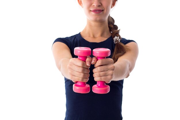 Foto mujer bonita joven en camiseta sosteniendo pesas rosadas frente a ella sobre fondo blanco en el estudio