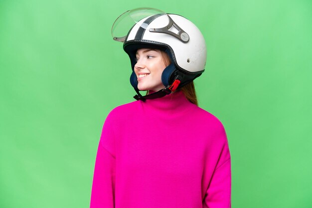 Mujer bonita joven con un casco de motocicleta sobre un fondo aislado de chroma key mirando hacia el lado